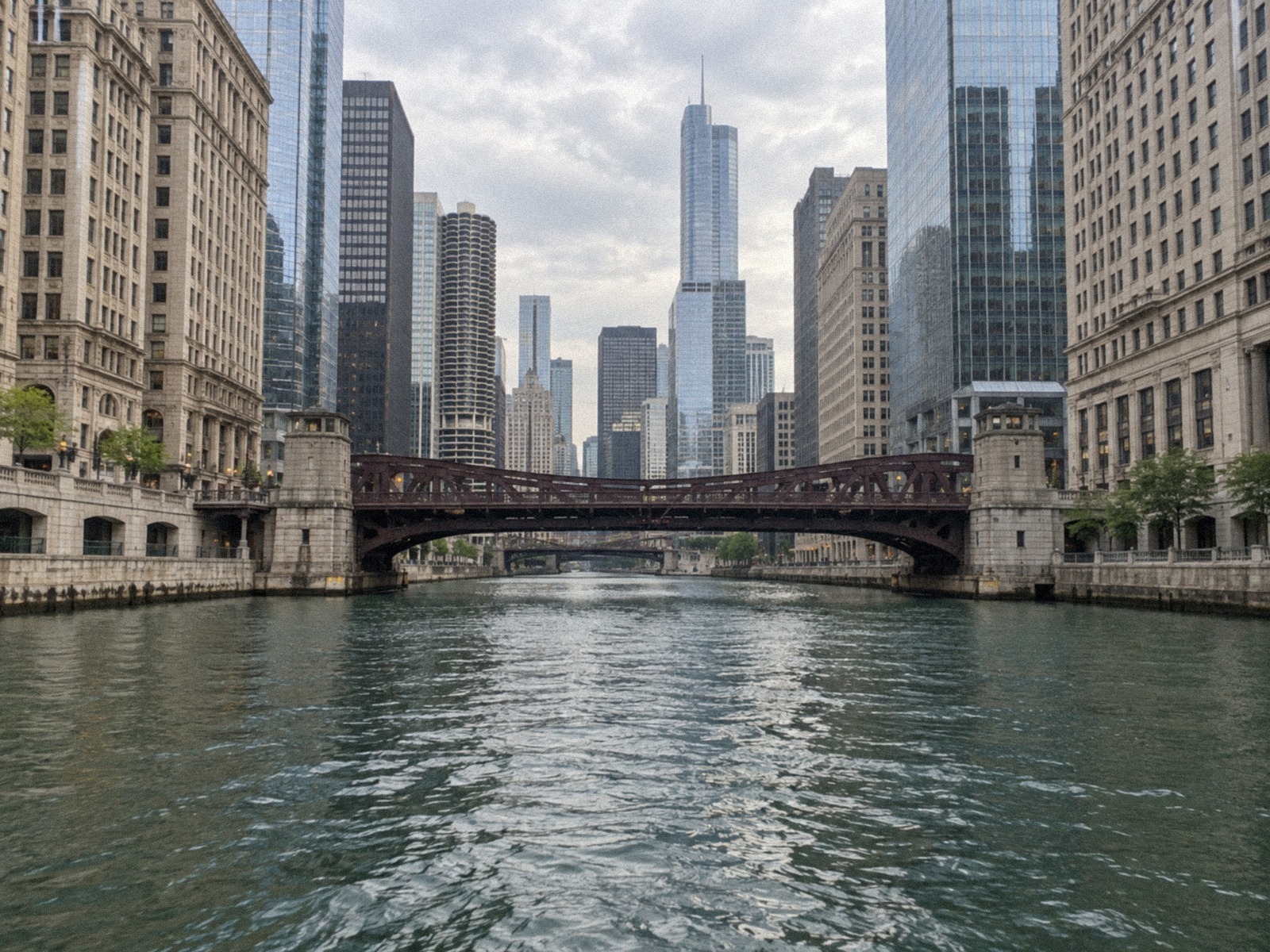 Chicago's river canyon seen from the water: masonry and glass towers flanking a steel bridge under an overcast sky.