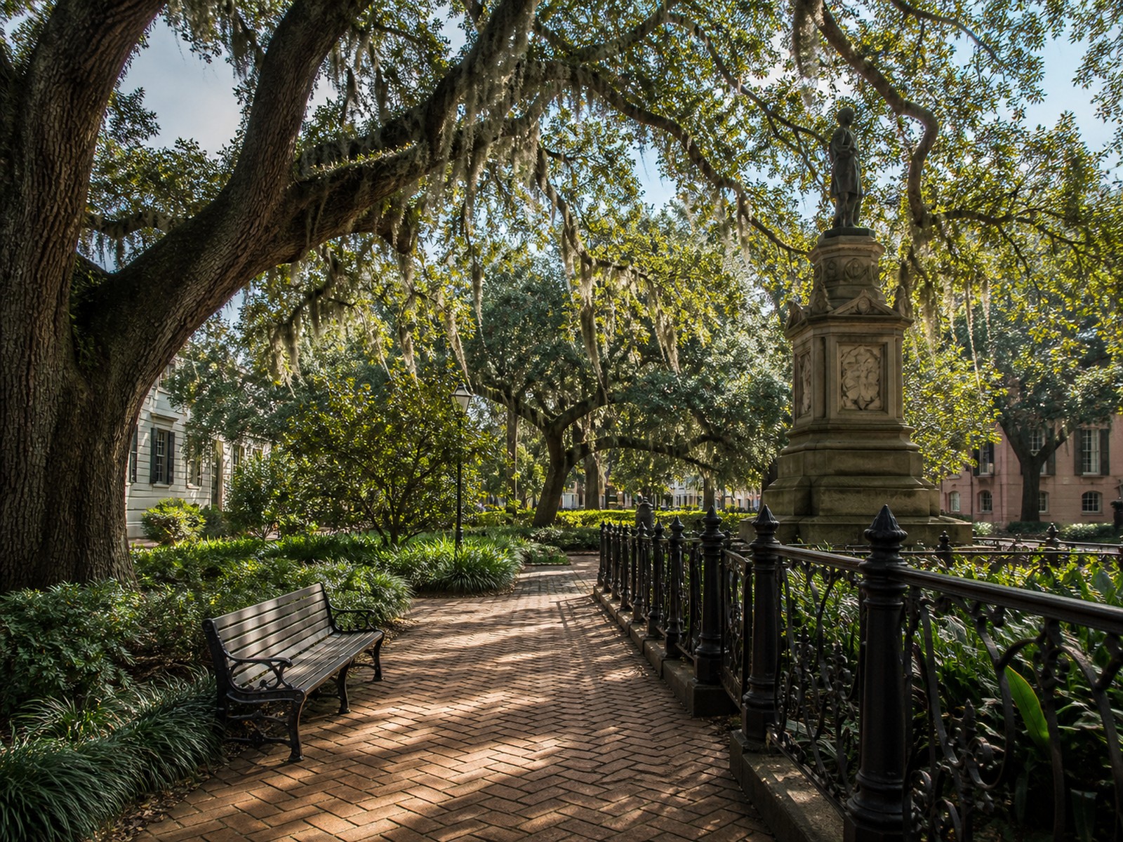 A brick path, wrought-iron rail, and live oaks in a quiet Savannah square.
